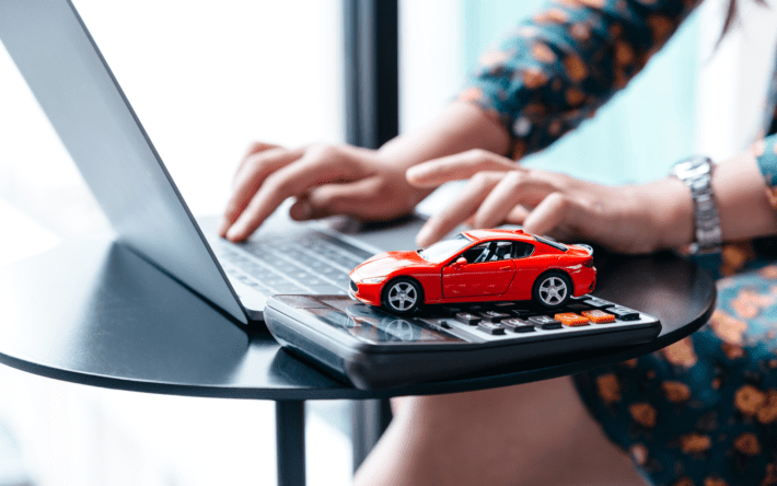 Mulher usando um computador com um carrinho de brinquedo posicionado sobre o teclado, simbolizando a busca por soluções para evitar a apreensão de veículos financiados.