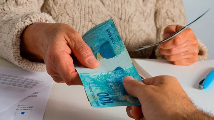 Pessoa emprestando uma nota de 100 reais para outra, simbolizando como conseguir empréstimo mesmo com o nome sujo.