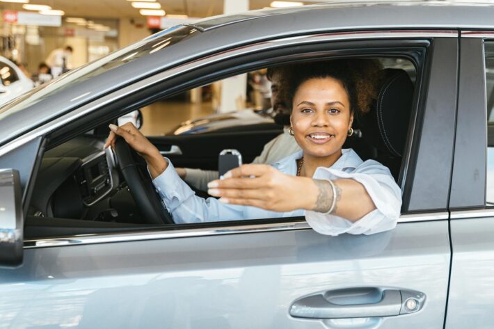 Mulher feliz dentro de um carro novo, segurando a chave do veículo recém-adquirido, após escolher o melhor financiamento.